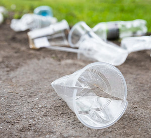 Heap of rubbish on the path, closeup. Empty used plastic cups and plastic bottles on blurred background, selective focus.Environmental pollution Weggeworfene Plastikbecher und Flaschen auf dem Boden