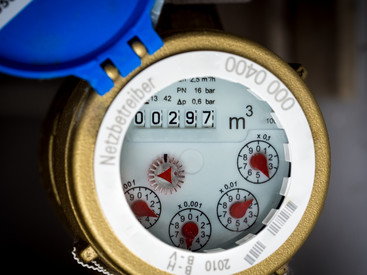 Informationen zum Trinkwasserverbrauch Das Bild zeigt einen Wasserzähler mit einem goldenen Gehäuse und einem blauen Deckel. Auf dem Zähler ist ein Verbrauch von 297 Kubikmetern (m³) ablesbar. Mehrere kleine rote Zeiger zeigen detaillierte Messwerte an.