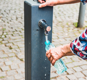 Frau füllt eine Flasche am Trinkwasserbrunnen auf