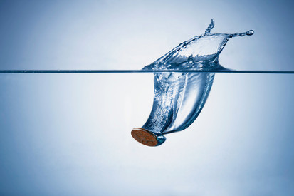 Informationen zum Wassercent Münze fällt ins Wasser, erzeugt großen Spritzer. Klares Wasser, blauer Hintergrund.